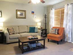 The spacious open living area has a ceiling fan, couch, tables, lamps and two chairs.